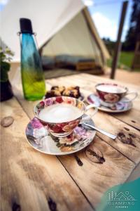 two cups of coffee on a wooden table with plates at Glamping Komarno in Jelenia Góra