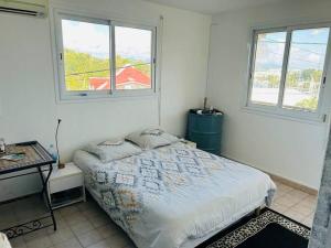 a bedroom with a bed and a table and two windows at Chambre d'hôtes Sunset Bas du Fort in Le Gosier