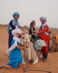 Eine Gruppe von Menschen, die auf dem Rücken eines Kamels reiten in der Unterkunft Zahra Luxury Desert Camp in Merzouga