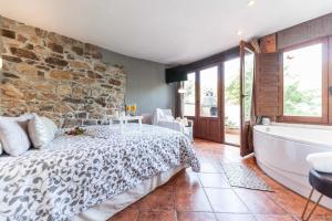 ein Schlafzimmer mit einer Steinmauer, einem Bett und einer Badewanne in der Unterkunft El Ablanu Senda del Oso in Proaza
