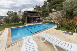 a swimming pool with two white chairs and a house at Refreshing Villa near Milas-Bodrum Airport in Gulluk