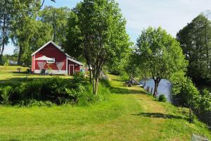 a red barn in a field next to a river at Riverside Bliss Cozy Apartment near Tvedestrand in Vegårshei