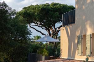 a white umbrella sitting next to a building with a tree at Hôtel L'Escalet in Ramatuelle