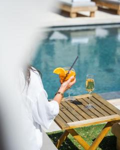 a woman holding a drink on a table next to a pool at Hôtel L'Escalet in Ramatuelle