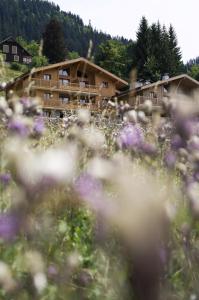 a building in the mountains with flowers in the foreground at CGH Résidences & Spas Les Chalets de Jouvence in Les Carroz d'Araches