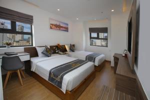 a bedroom with two beds and a desk and two windows at Skylight Hotel Nha Trang in Nha Trang