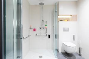 ein weißes Bad mit einer Dusche und einem WC in der Unterkunft Moxy Dresden Neustadt in Dresden