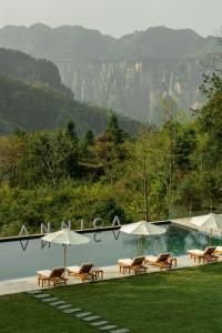 a pool with chairs and umbrellas next to a mountain at ANNICA Villa in Zhangjiajie