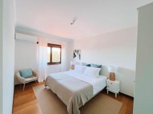 a white bedroom with a bed and a chair at Just Like Home - Casa Glória in Cristelo
