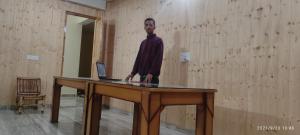 a man standing at a table with a laptop at OYO Kamal Guest House Tirthan in Banjār