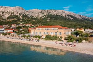 a building on a beach with chairs and the water at Hotel Dobrovit in Baška