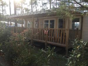 a wooden cabin with a porch in a yard at Plage de Contis, Camping SIBLU 3*, parc aquatique, piscines chauffées. in Saint-Julien-en-Born