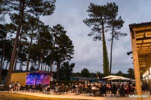 una folla di persone sedute ai tavoli di fronte a un palco di Plage de Contis, Camping SIBLU 3*, parc aquatique, piscines chauffées. a Saint-Julien-en-Born