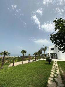 a white house with palm trees and a grass field at Villa Marina Hills - Tamuda Bay in Jebel Zemzem