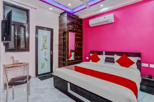 Habitación de color rosa con cama y escritorio. en Super OYO The Prima Residency en Ghaziabad