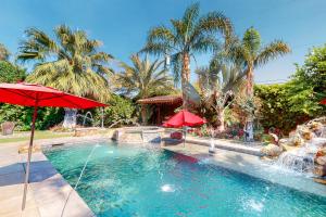a swimming pool with two umbrellas and a fountain at Fred Waring Dreams in Palm Desert