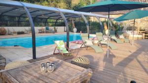 una terraza con sillas, una sombrilla y una piscina en Le Manoir des Pélies Gîte et Chambres d'hôtes de charme à 7kms de Conques Spa, Piscine, Rivière, Thermes de Cransac, en Conques