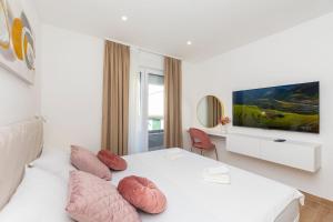 a white bedroom with a bed with pillows and a tv at New Apartment White Angel in Duće