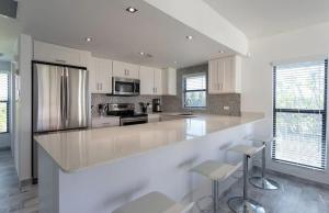 a large white kitchen with a large counter and stools at Beach Living at Villas Pappagallo BLES in West Bay