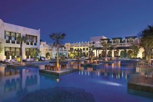 ドーハにあるSharq Village & Spa, a Ritz-Carlton Hotelの夜間のヤシの木と建物のある大きなプール