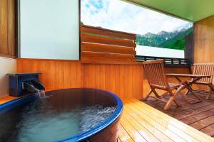a hot tub in a room with a table and a chair at Hotel Hotaka in Takayama