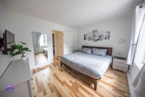 a white bedroom with a bed and a wooden floor at Le Petit Manoir - Quartz in Lac-Simon