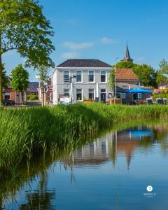 a house next to a river with tall grass at Hotel Restaurant Toxopeus in Anjum