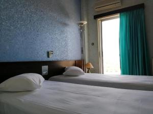 a bedroom with two beds and a window with green curtains at HOTEL ALEXANDROS in Loutraki
