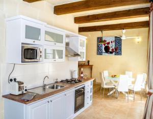 una cocina con armarios blancos y una mesa con sillas. en Karmnu Holiday Farmhouse, en Għasri