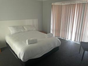 Un dormitorio con una cama con sábanas blancas y una ventana. en Frangipani, en Albany