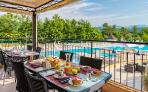 a table with food on a balcony with a view of a pool at Lagrange Vacances Domaine de Fayence in Fayence