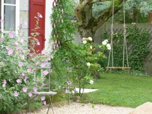 un jardín con una puerta roja, flores y un columpio en Les volets rouges en Sémoy