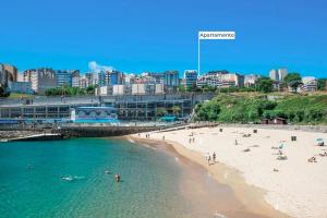 a beach in front of a city with people in the water at Apartamento Torre de Hércules in A Coruña