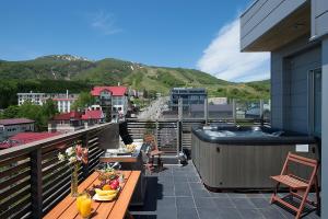 a balcony with a hot tub and tables on a building at The Setsumon in Niseko