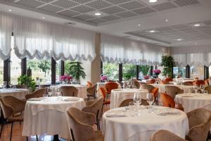 a restaurant with white tables and chairs and windows at Savoy Beach Hotel & Thermal Spa in Bibione
