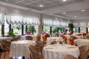 a restaurant with white tables and chairs and windows at Savoy Beach Hotel & Thermal Spa in Bibione