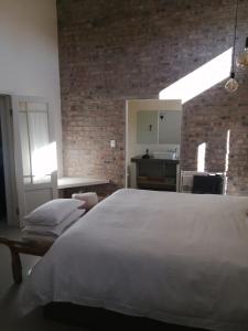 a bedroom with a white bed and a brick wall at Serendipity Cottage in Prince Albert