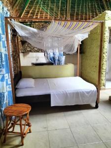 Kikambala Eco Villas في مومباسا: غرفة نوم مع سرير مع مظلة ومقعد