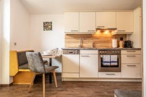 a kitchen with white cabinets and a table and a chair at Alpha Apartments in Schwarzach im Pongau