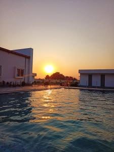 a swimming pool with the sun setting in the background at Lakshya Resort in Gorakhpur