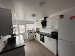 a large kitchen with white appliances and black counter tops at Modern & Spacious Terrace House in Friern Barnet