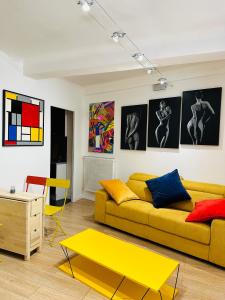 a living room with a yellow couch and some paintings at POP appART Appartement Artiste 200 m du centre ville Parking privé gratuit in Avignon