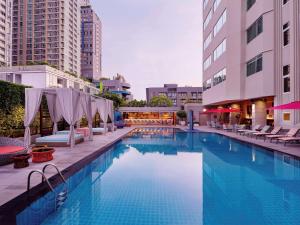 Mercure Bangkok Sukhumvit 11 في بانكوك: مسبح كبير وبه كراسي ومظلات بجوار مباني