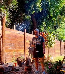 un hombre mayor parado en un jardín junto a una valla en Cabaña Jano en Posadas