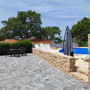 una pared de piedra con sillas y una sombrilla junto a una piscina en Apartman Dadić, en Malinska