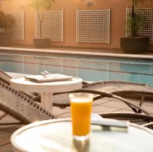 a glass of orange juice sitting on a table next to a pool at Intercity Cuiabá in Cuiabá