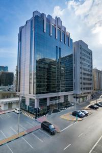 a large glass building with cars parked in a parking lot at Kingsgate Hotel by Millennium in Abu Dhabi