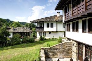 una casa bianca con un prato accanto a un edificio di Strannopriemnitsa Guest House a Bozhentsi