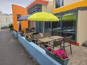 patio ze stołami i krzesłami oraz żółtym parasolem w obiekcie KYRIAD DIRECT LYON NORD - Dardilly w mieście Dardilly