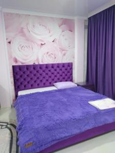 Un dormitorio con una cama morada con una pintura de rosas. en Гостевой дом ЛОНТАНА, en Gagra